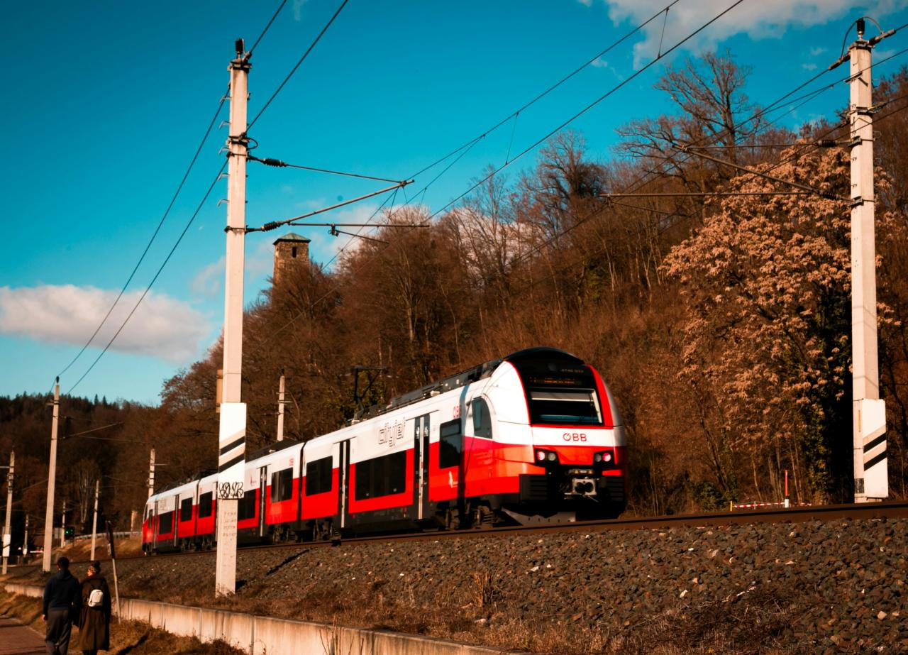 A red and white train travels on tracks near trees.